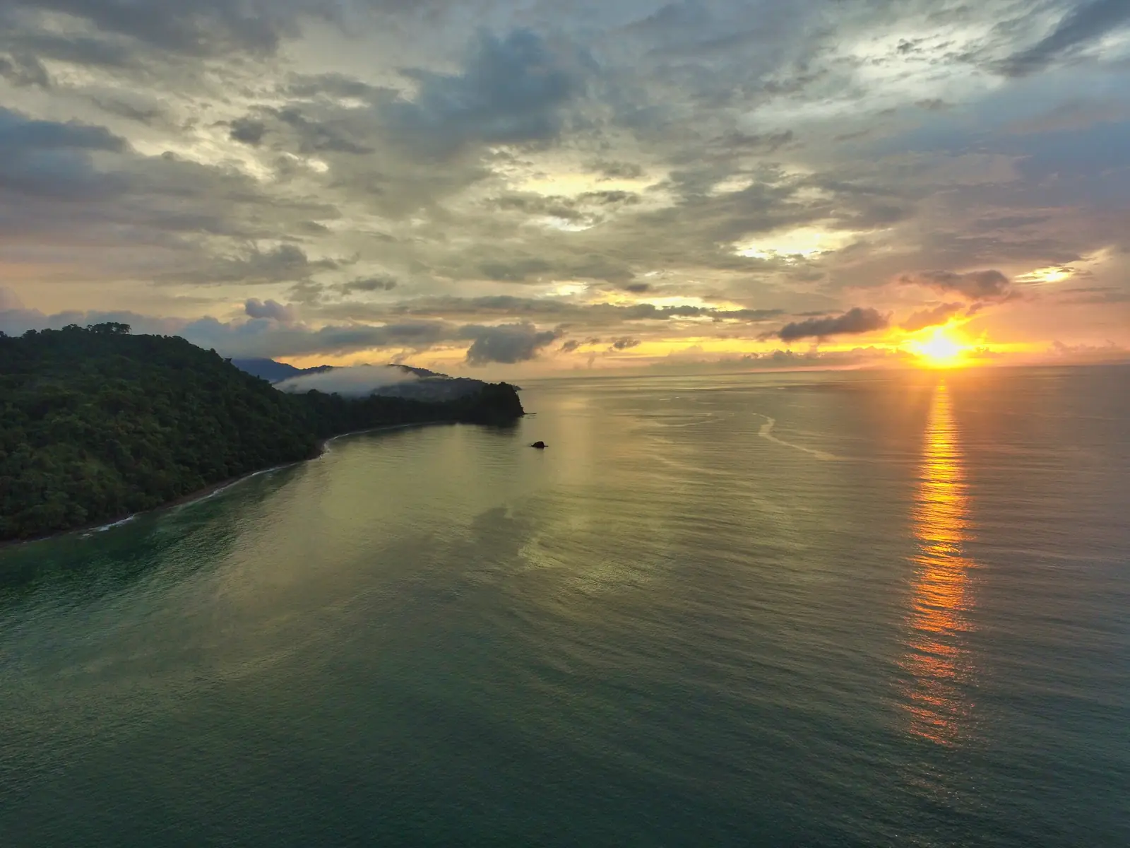 Sunset over calm water beside a forested headland