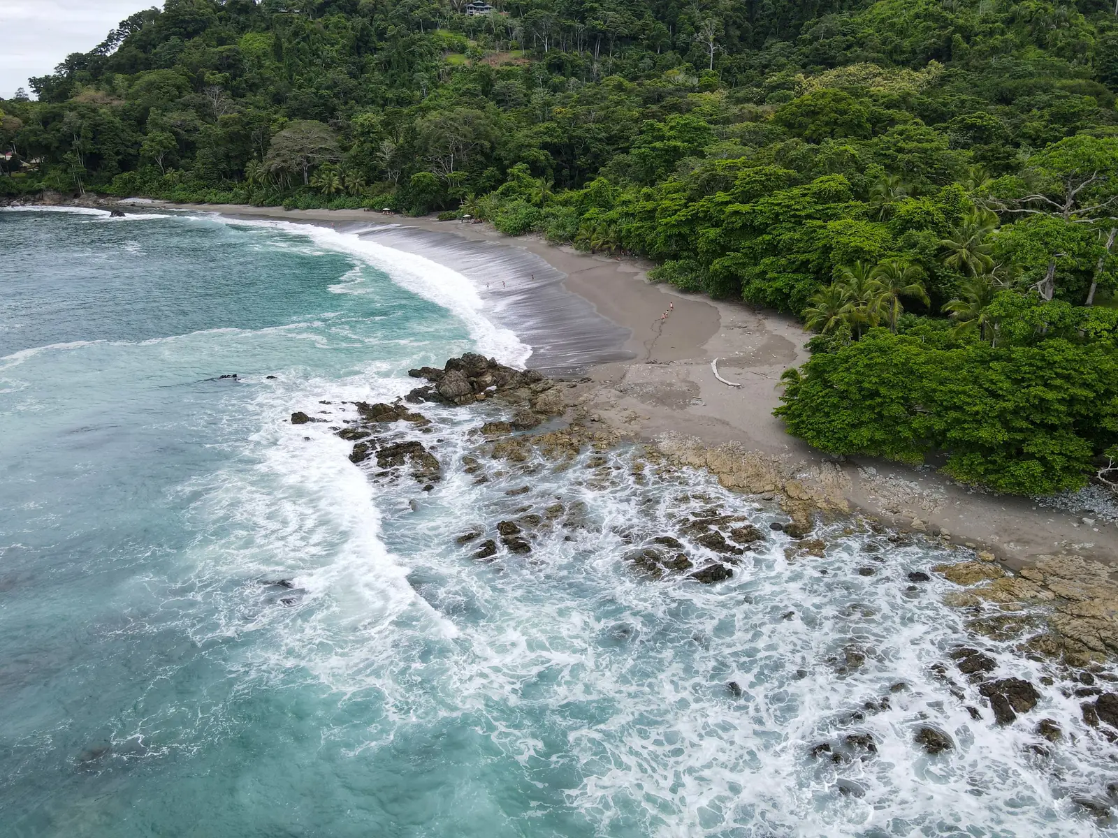 Aerial view of waves breaking over rocks below a forested shore